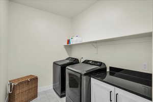 Washroom featuring independent washer and dryer, light tile patterned flooring, and cabinet space