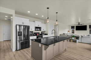 Kitchen featuring black appliances, decorative light fixtures, open floor plan, an island with sink, and white cabinets