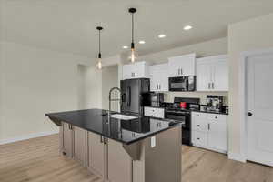 Kitchen featuring black appliances, a kitchen island with sink, decorative light fixtures, recessed lighting, and white cabinets