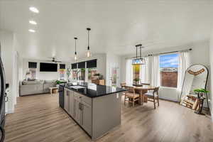 Kitchen featuring decorative light fixtures, gray cabinetry, a kitchen island with sink, light wood-type flooring, and open floor plan