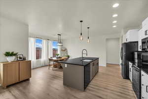 Kitchen with a kitchen island with sink, black appliances, white cabinetry, pendant lighting, and light wood finished floors