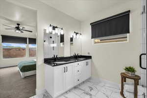 Full bath with ensuite bath, double vanity, light marble finish floors, and a ceiling fan