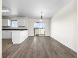 Kitchen featuring dark countertops, white cabinetry, pendant lighting, dark wood-style flooring, and a peninsula