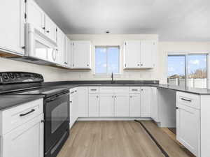 Kitchen featuring black range with electric stovetop, dark countertops, white cabinets, and white microwave