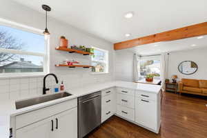 Kitchen with a peninsula, white cabinetry, hanging light fixtures, stainless steel dishwasher, and open floor plan