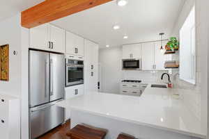 Kitchen with a peninsula, stainless steel appliances, white cabinets, pendant lighting, and light stone counters