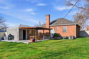 Back of property featuring a patio, a chimney, brick siding, and a shingled roof