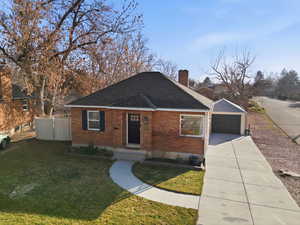 View of front of house featuring brick siding, driveway, a chimney, and a shingled roof