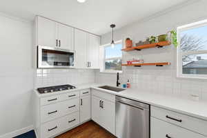 Kitchen with pendant lighting, stainless steel appliances, white cabinetry, and dark wood finished floors