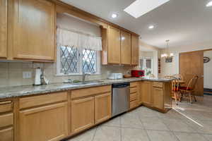 Kitchen with skylights, a peninsula, stainless steel dishwasher, light stone countertops, and decorative light fixtures