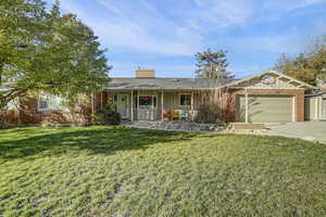Ranch-style house with board and batten siding, brick siding, a front yard, and driveway