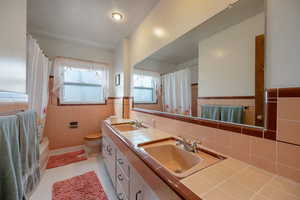 Main level Full bathroom featuring tile walls, double vanity, light tile patterned floors, and shower / bath combo