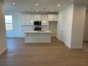 Kitchen featuring white cabinetry, decorative backsplash, appliances with stainless steel finishes, a kitchen island with sink, and recessed lighting