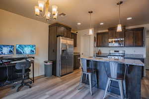 Kitchen with dark brown cabinetry, a breakfast bar, stainless steel appliances, light stone countertops, and recessed lighting