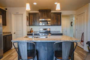 Kitchen featuring dark brown cabinetry, decorative light fixtures, stainless steel appliances, and light stone countertops