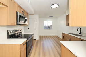 Kitchen with stainless steel appliances, light stone counters, light wood-style floors, a textured ceiling, and light brown cabinets