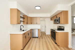 Kitchen with stainless steel appliances, open shelves, light wood finished floors, light stone counters, and a textured ceiling