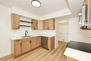 Kitchen featuring open shelves, light wood-style flooring, stainless steel appliances, a textured ceiling, and light wood finish cabinets