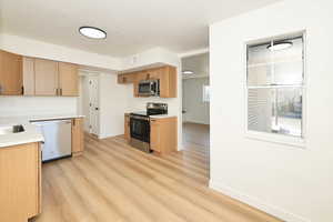 Kitchen featuring appliances with stainless steel finishes, light countertops, a textured ceiling, light wood-style flooring, and light brown cabinets