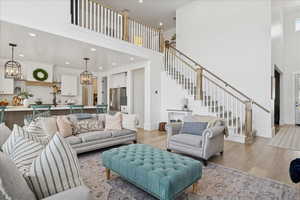 Living room featuring light wood-style floors, a high ceiling, a chandelier, stairway, and recessed lighting