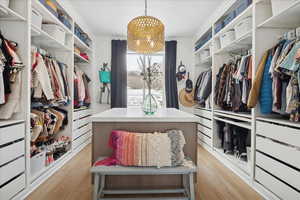 Walk in closet with a chandelier and light wood-type flooring