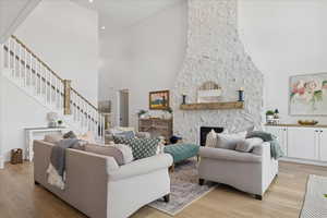 Living area with a high ceiling, a stone fireplace, light wood-style flooring, stairs, and recessed lighting