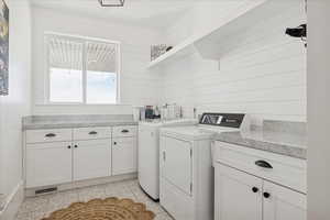 Washroom with washing machine and clothes dryer, cabinet space, wooden walls, and light tile patterned floors