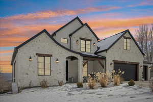 View of front of home with stone siding, a garage, covered porch, and stucco siding
