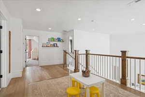 Hallway with an upstairs landing, light wood-type flooring, and recessed lighting