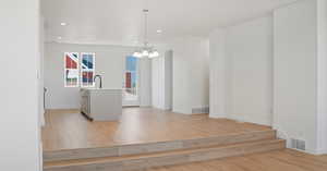 Kitchen with light wood-type flooring, hanging light fixtures, light countertops, an island with sink, and a chandelier