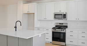 Kitchen with appliances with stainless steel finishes, white cabinetry, a center island with sink, light stone counters, and light wood finished floors