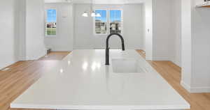 Kitchen view of a kitchen island with sink, decorative light fixtures, light wood finished floors, light stone counters, and a chandelier