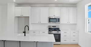 Kitchen with stainless steel appliances, white cabinetry, recessed lighting, light stone counters, and plenty of natural light