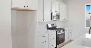 Kitchen featuring appliances with stainless steel finishes, white cabinetry, light stone counters, and light wood finished floors