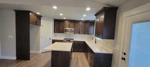 Kitchen featuring dark brown cabinetry, light wood-type flooring, recessed lighting, a center island, and appliances with stainless steel finishes