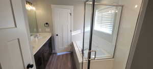 Master Bathroom with double vanity, a bath, a shower stall, and dark wood-type flooring