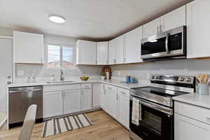 Kitchen with appliances with stainless steel finishes, white cabinets, light wood-style floors, a textured ceiling, and light stone counters