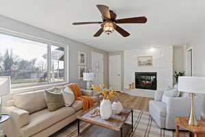 Living area featuring a large fireplace, a ceiling fan, wood finished floors, and a textured ceiling