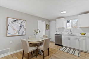 Kitchen featuring white cabinets, dishwasher, and light wood-style floors