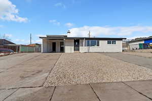 Ranch-style home featuring concrete driveway, brick siding, an attached carport, a chimney, and a porch