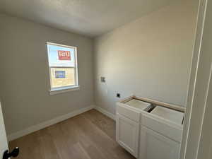 Laundry area with a textured ceiling, light wood-type flooring, hookup for a washing machine, hookup for an electric dryer, and cabinet space