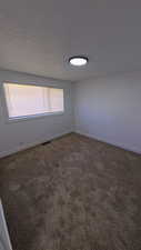Spare room featuring dark colored carpet and baseboards