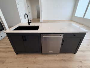 Kitchen with light wood-type flooring, a kitchen island with sink, dishwasher, and dark cabinetry