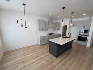 Kitchen featuring gray cabinets, hanging light fixtures, tasteful backsplash, a kitchen island with sink, and recessed lighting