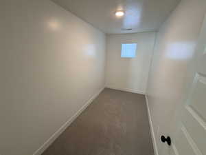 Carpeted spare room featuring a textured ceiling and baseboards