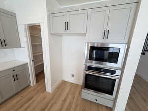 Kitchen with appliances with stainless steel finishes, gray cabinets, light wood-type flooring, decorative backsplash, and light stone counters