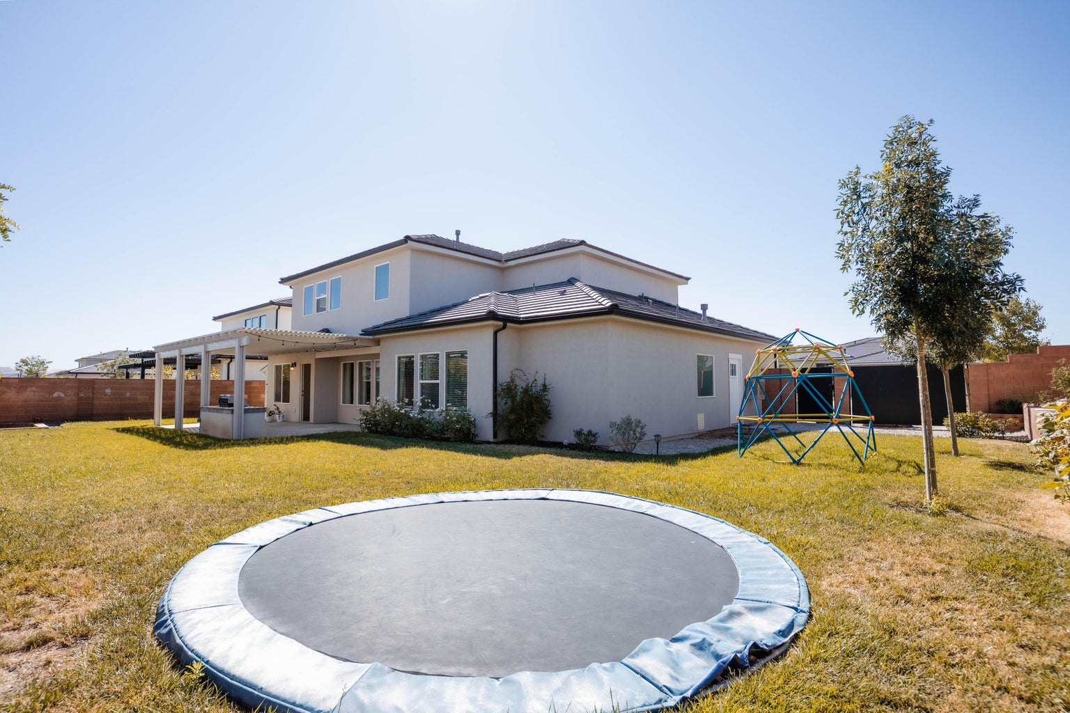 Back of house featuring a trampoline, a fenced backyard, a patio area, a pergola, and stucco siding