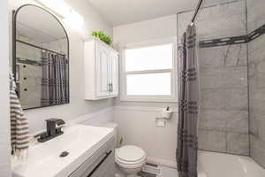 Full bathroom featuring a wainscoted wall, vanity, and shower / bathtub combination with curtain