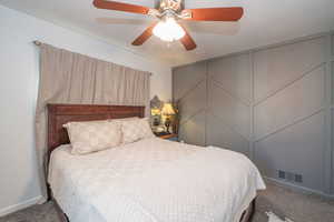 Carpeted bedroom featuring a ceiling fan and a decorative wall