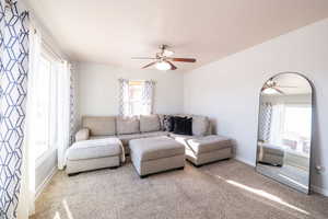 Carpeted living room featuring a ceiling fan and baseboards